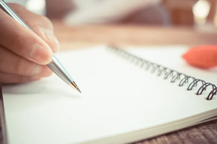 Hand with silver pen writing on a notebook.