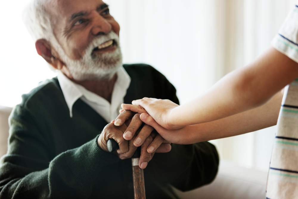 Older person holds support cane while a child places hands affectionately on the older person's