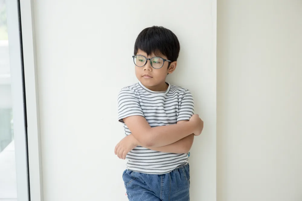 Kid in white stripped t-shirt and glasses with crossed arm across his chest.