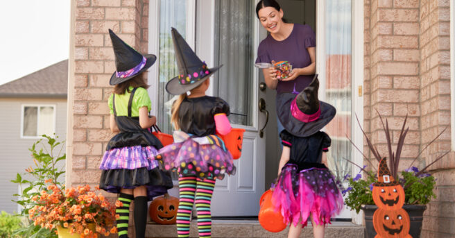 3 kids dressed in costumes at door with mom treats children with candy.