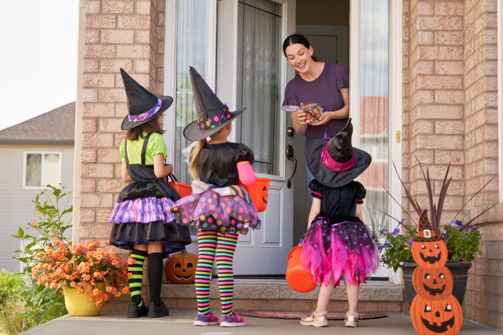 3 kids dressed in costumes at door with mom treats children with candy.