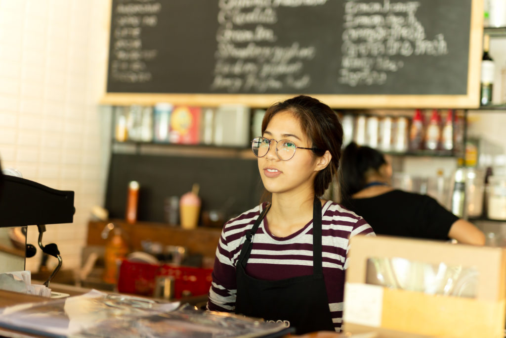 Teen girl wearing an apron behind the counter at a coffee shop