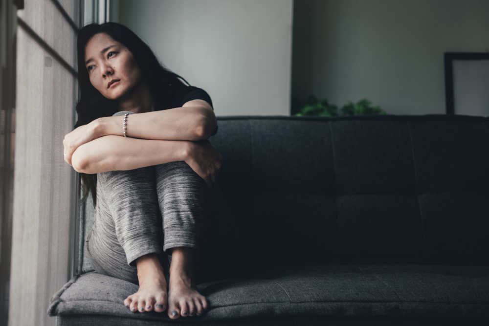 Person wrapping their arms around their legs in a curled position with their head resting on the wall