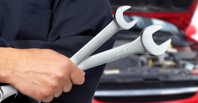 Person holds two wrenches in front of a car