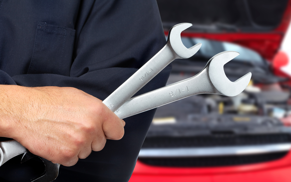 Person holds two wrenches in front of a car