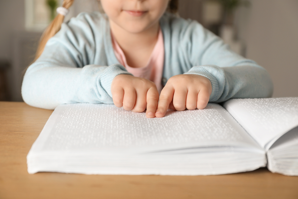 Blind child reading book written in Braille at table, closeup.