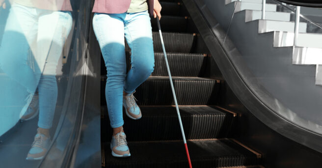 Person descending an escalator with a white cane