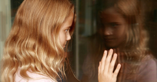 Young girl facing outside with her reflection of herself in the window. 