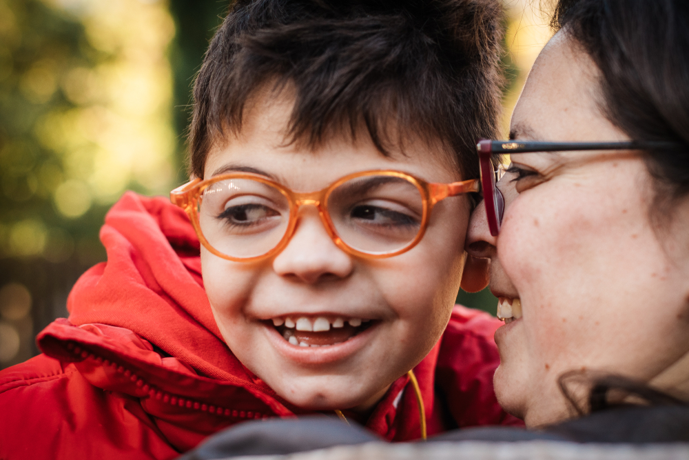 A boy wearing glasses smiling with his mom.