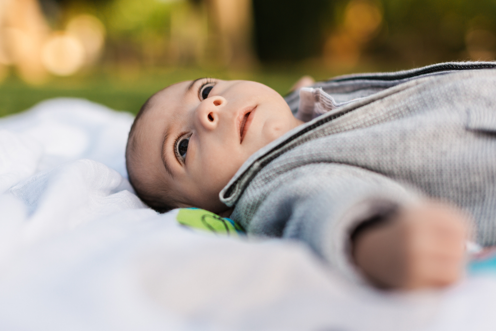A baby laying on a blanket outside looking off to the distance. 