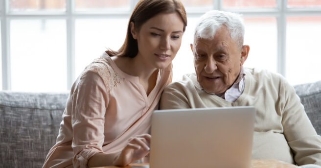 Person teaching older adult to use a laptop computer