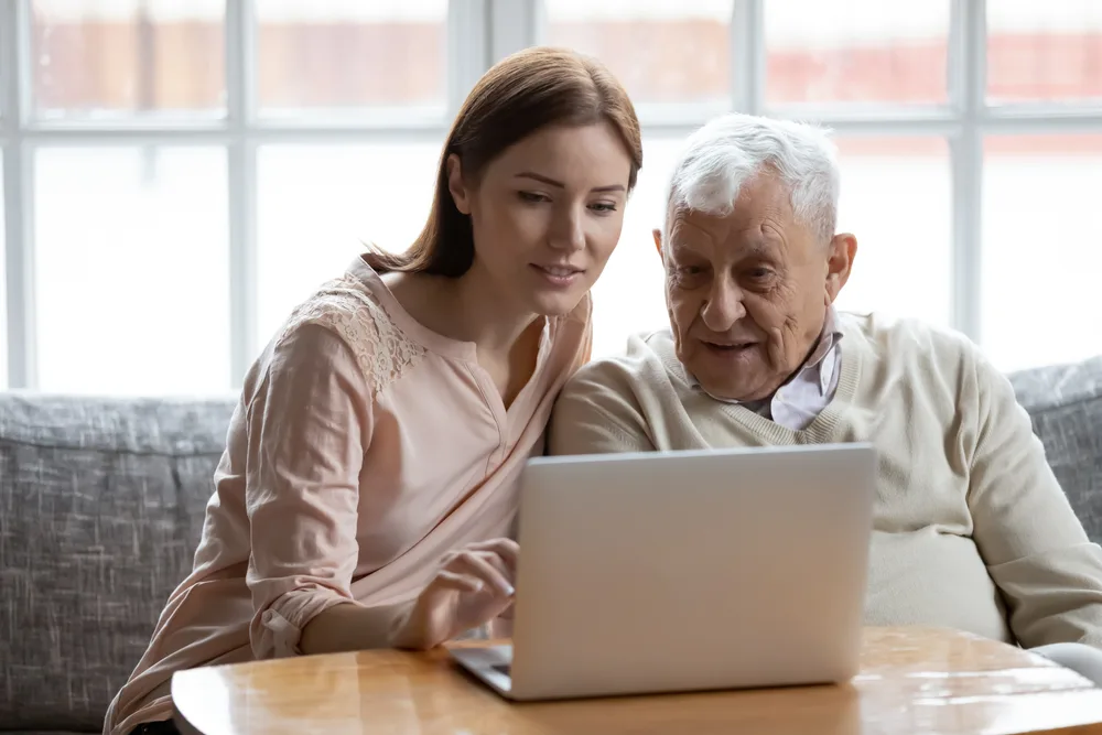 Person teaching older adult to use a laptop computer