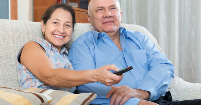 Older couple sitting on a couch holding a remote control