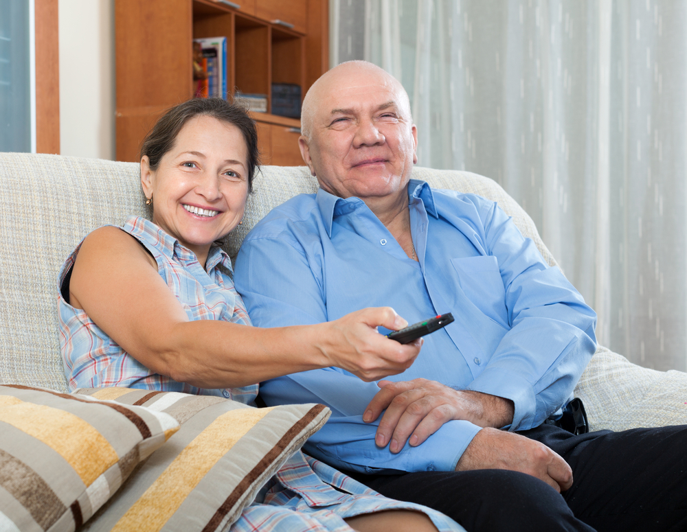 Older couple sitting on a couch holding a remote control