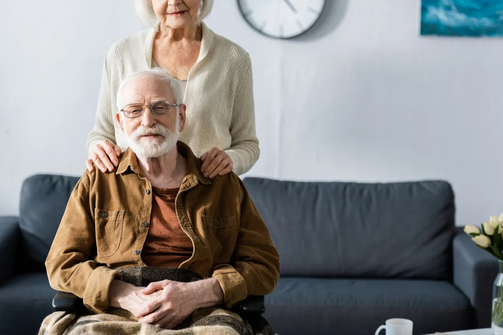 Older person sits in a wheelchair with a loved one behind them