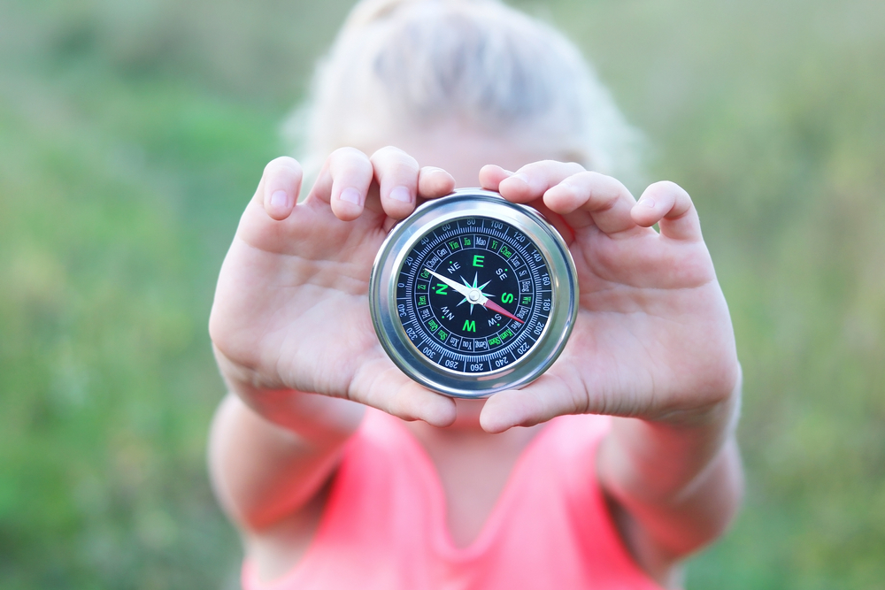 Round compass in child’s hand on green grass background. 