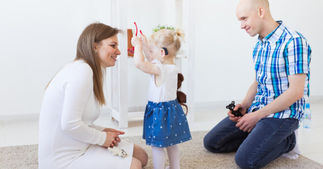 Child with hearing aids playfully gives eyeglasses to an adult