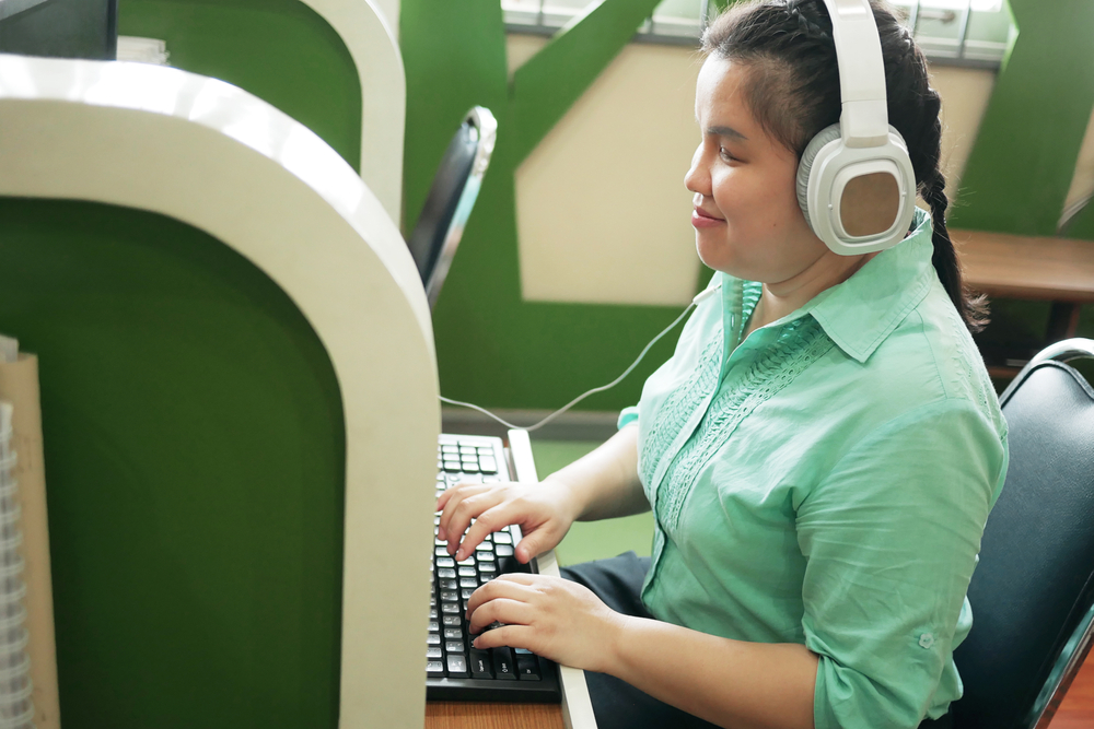 happy woman in headphone typing on computer keyboard working in workplace office.