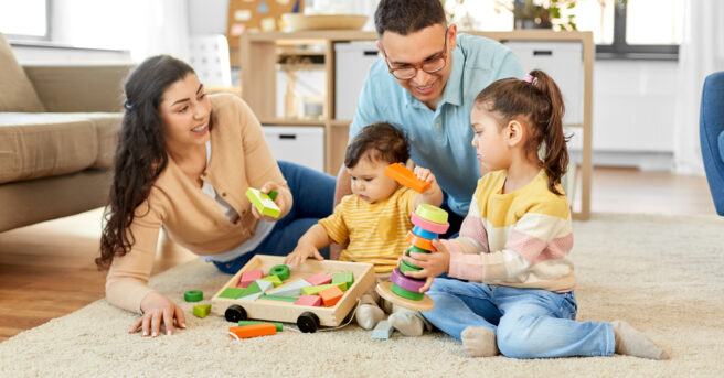Happy mother, father, little daughter and baby son playing with wooden toys at home.