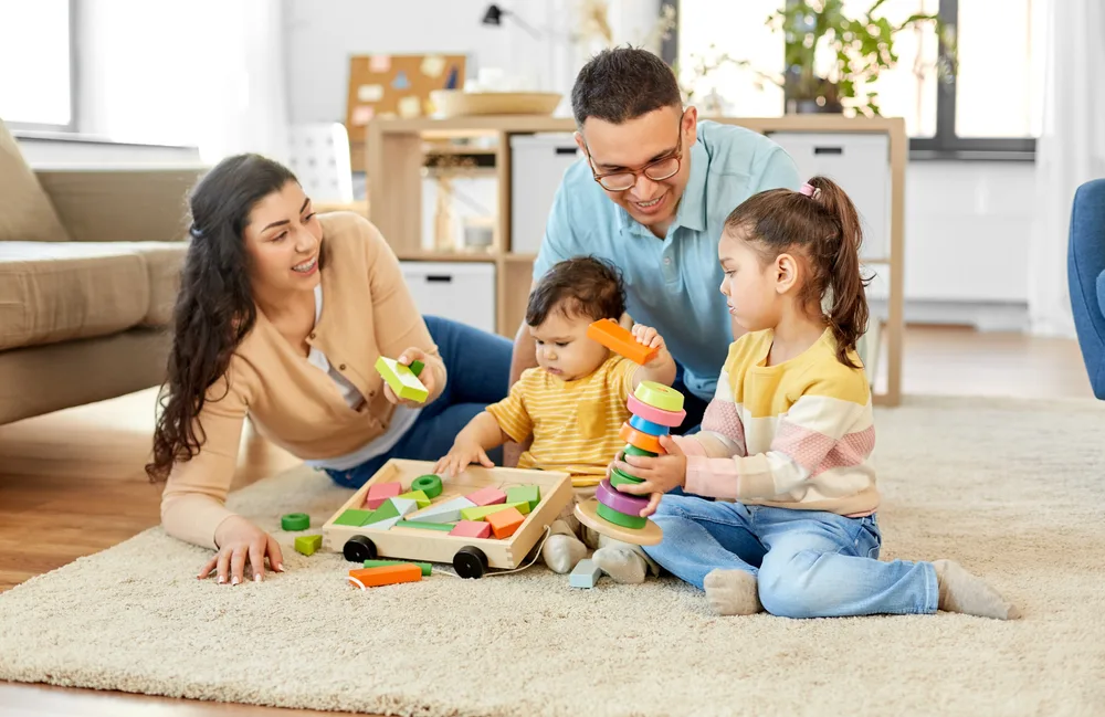 Happy mother, father, little daughter and baby son playing with wooden toys at home.