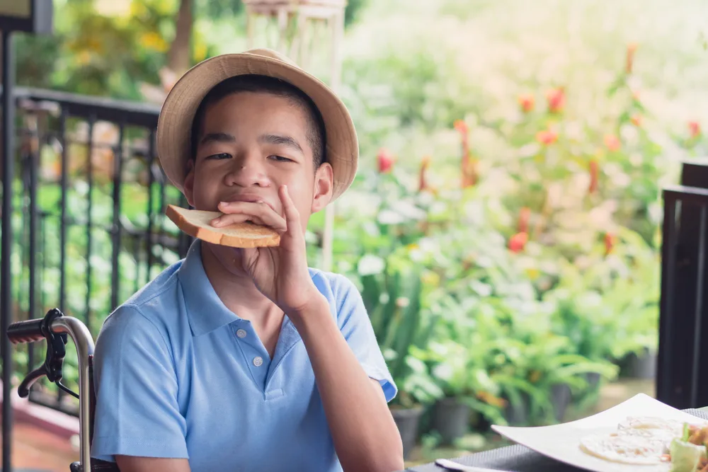 A child with multiple disabilities in a wheelchair eating breakfast independently.