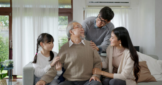 Older man wearing eyeglasses surrounded by family of various ages