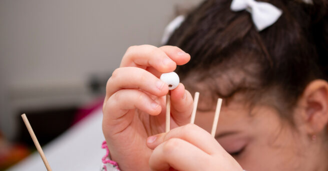 A young girl putting a bead onto a peg.