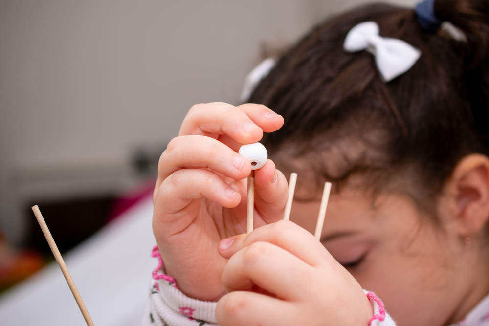 A young girl putting a bead onto a peg.