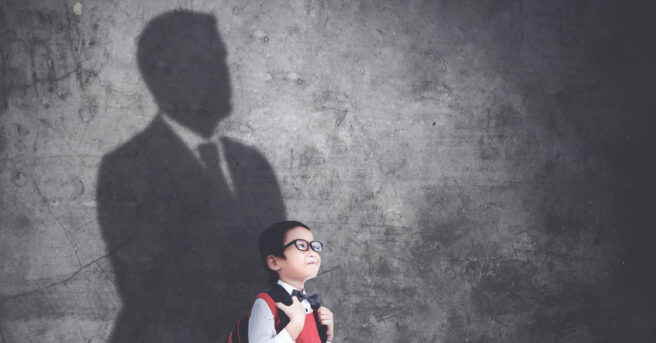 Happy schoolboy standing with his shadow on the wall while imagining be a businessman.