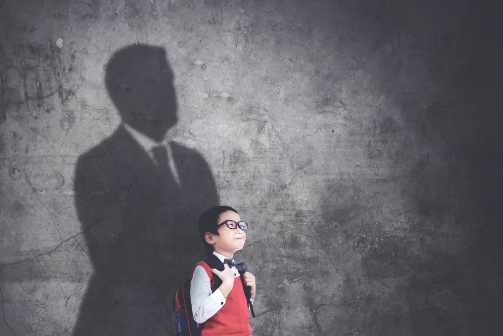 Happy schoolboy standing with his shadow on the wall while imagining be a businessman.