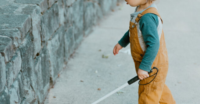 Toddler exploring concrete wall with white cane.