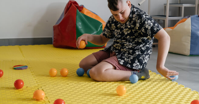 A boy sitting on a sensory mat playing with various balls.