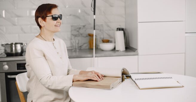 Woman sitting in kitchen reading braille.