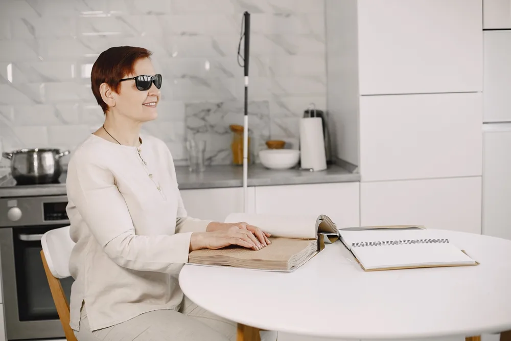 Woman sitting in kitchen reading braille.