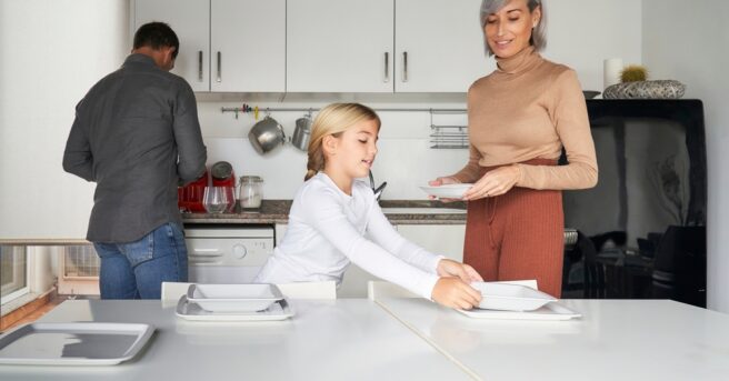 Family consisting of father, mother and daughter setting the table to eat in the kitchen.