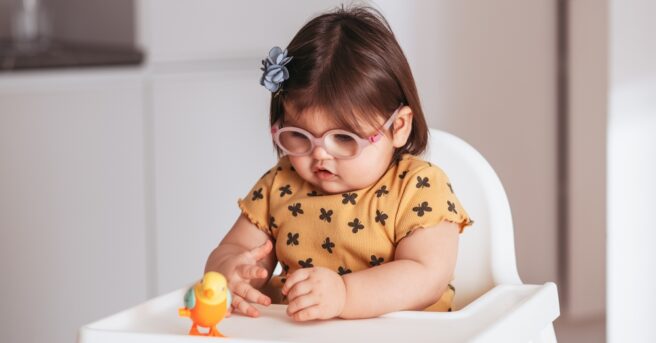 A little baby girl wearing eyeglasses playing with a toy.