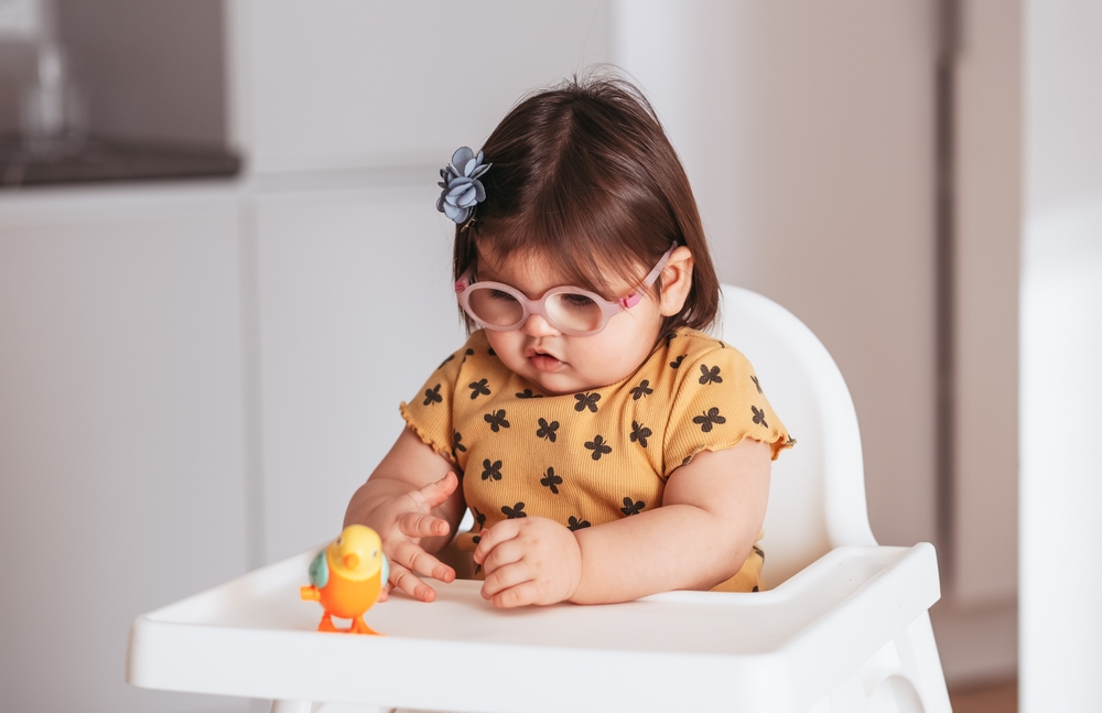 A little baby girl wearing eyeglasses playing with a toy.