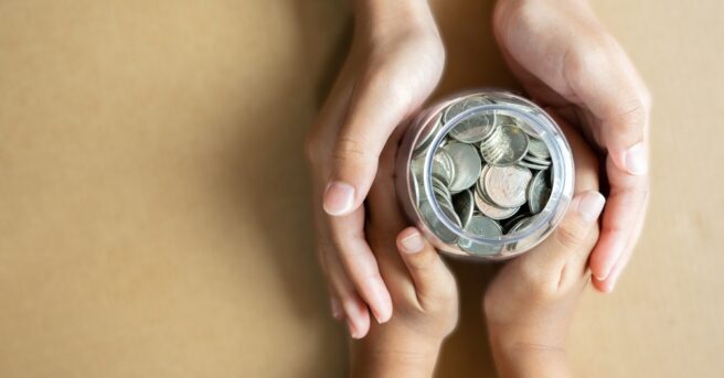 Kid hands holding coins in a jar together as saving concept for family or education.