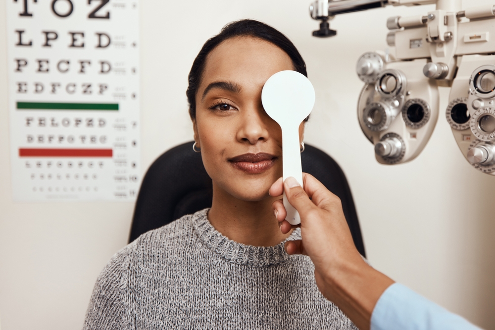 Woman in eye doctors office with a cover on one eye and an eye chart in the background
