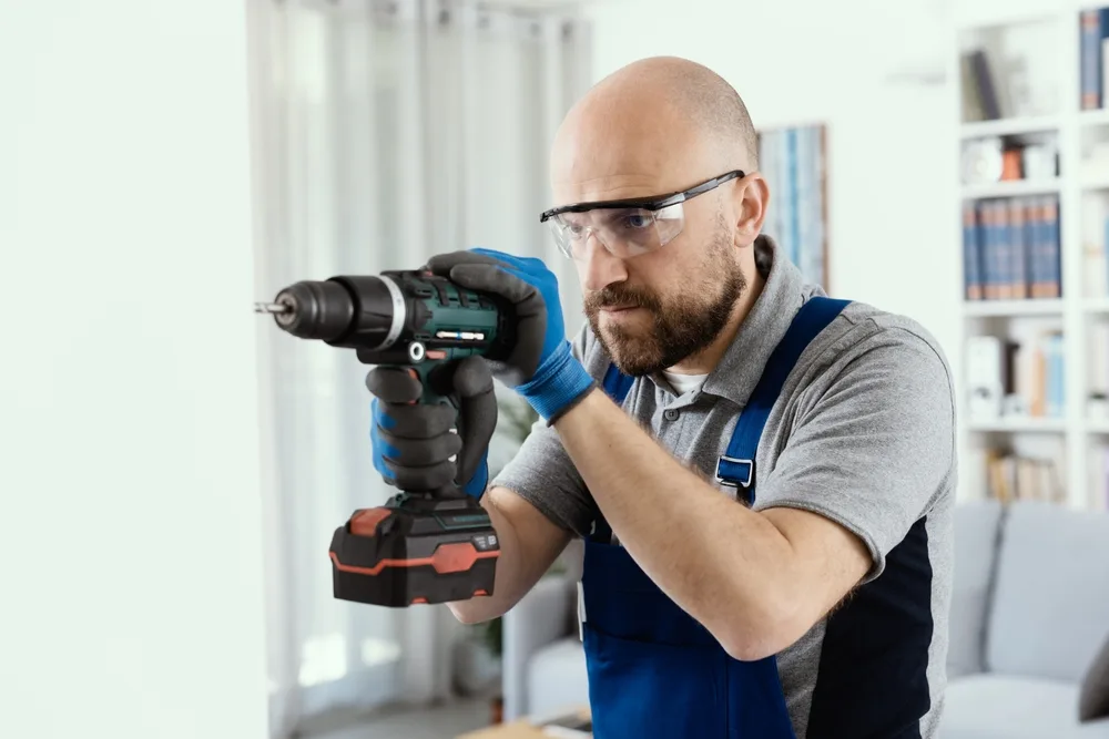 Person wearing safety goggles and drilling a hole into a wall