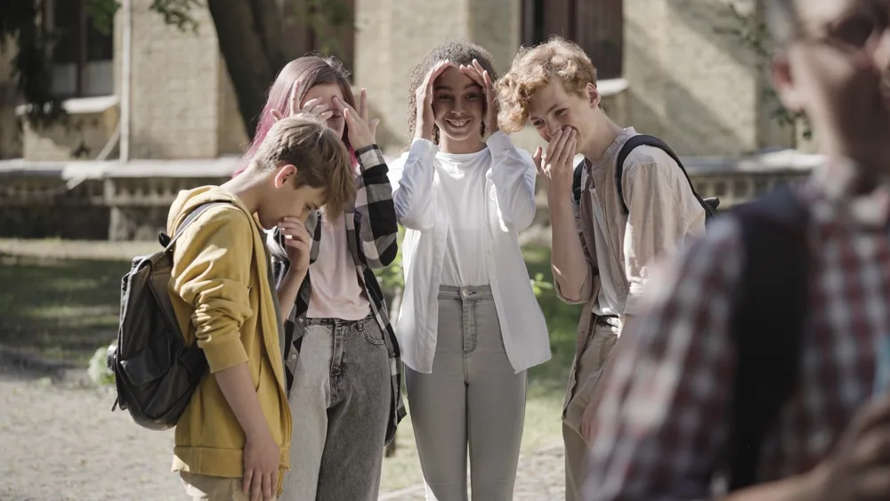 Group of school children gossiping and laughing at insecure classmate.