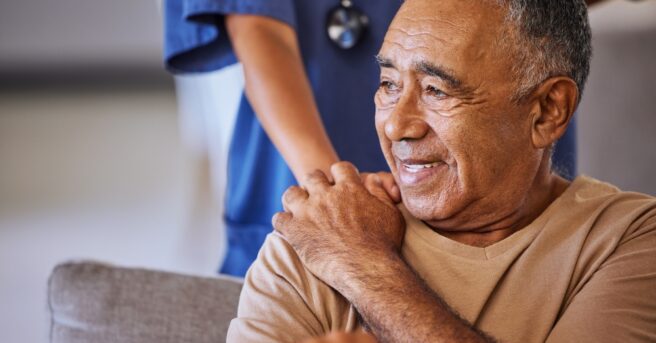 Older person smiles with nurse in the background