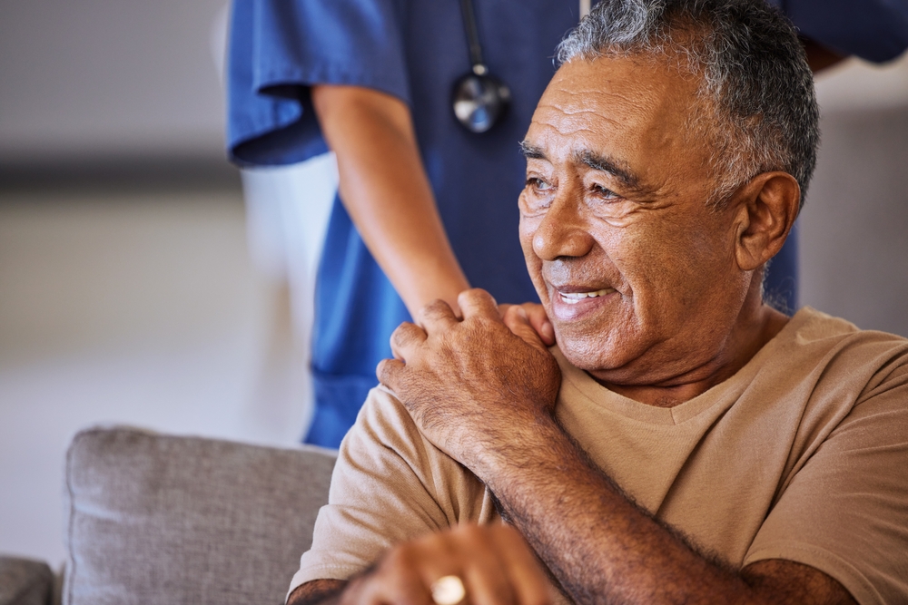 Older person smiles with nurse in the background