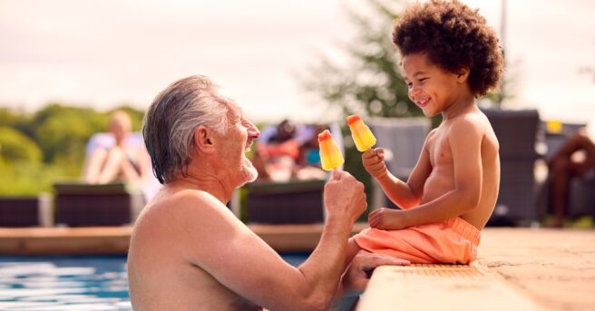 Grandparent and grandchild eat popsicles in the pool
