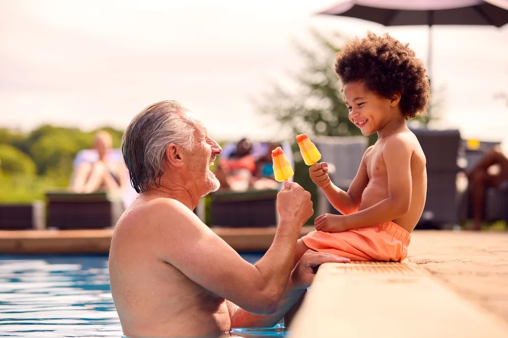 Grandparent and grandchild eat popsicles in the pool