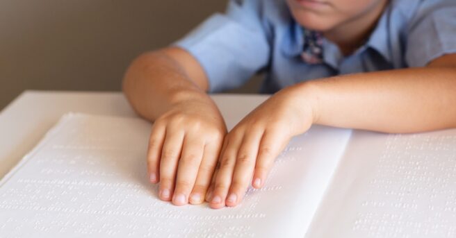 A boy sitting at a desk reading braille.