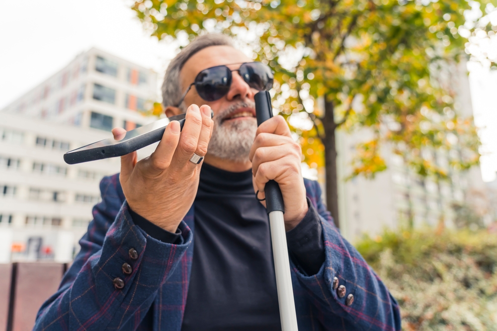 Person with graying hair uses white cane and smartphone