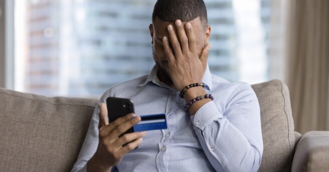 Person holding a phone and credit card while their other hand is placed over their face in overwhelm or frustration