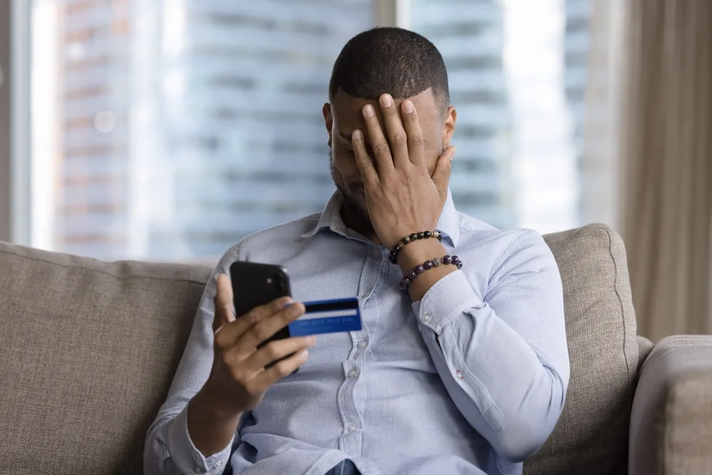 Person holding a phone and credit card while their other hand is placed over their face in overwhelm or frustration