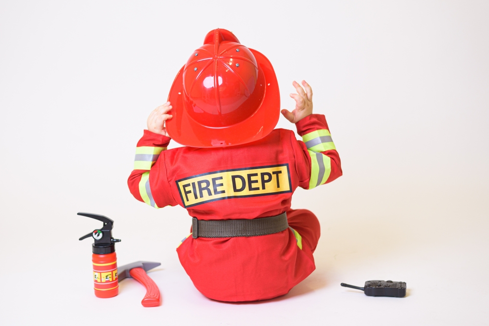 Little toddler playing with fire truck equipment and dressed up in fireman outfit. 